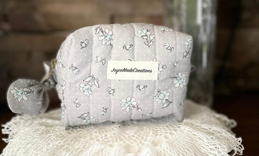 Gray floral-patterned pouch on a lace doily with flowers in the background