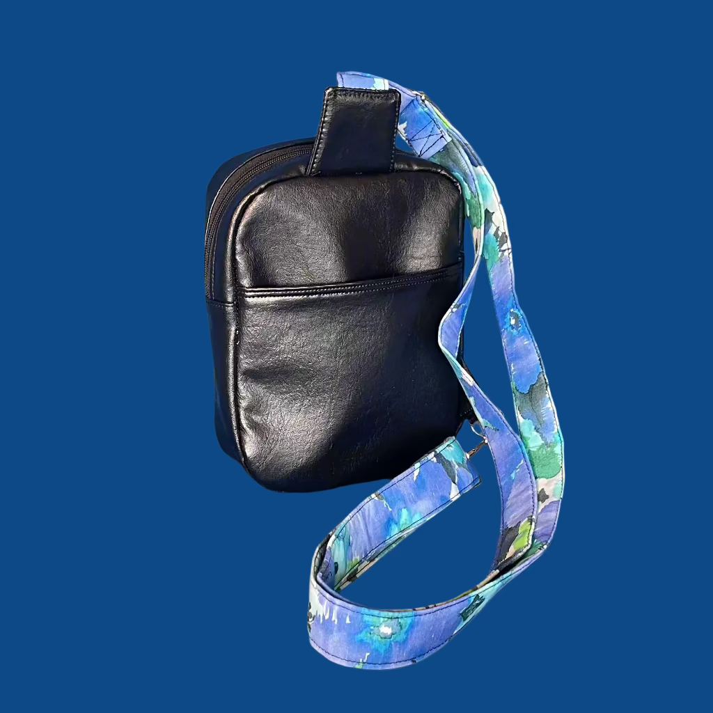 Featuring the back of the black reclaimed vinyl sling bag.  Made from scraps of car interior. Accented with blue and green watercolor cotton fabric accent, lining and strap. Back slip pocket.